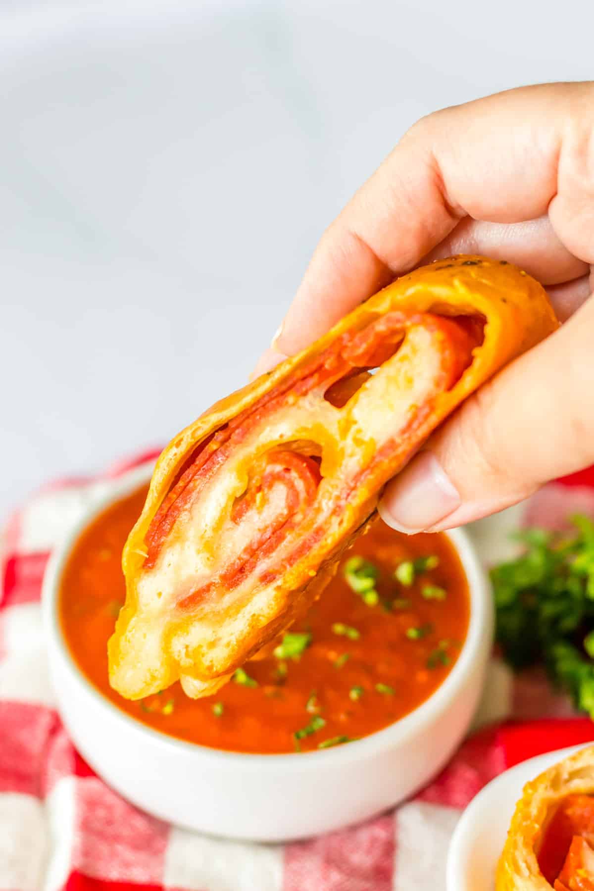 Slice of pepperoni bread being dunked in small bowl of marinara sauce.