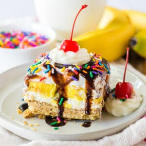 No bake banana split dessert with a graham cracker crust; layers of sweetened cream cheese, banana pudding, and Cool Whip; and topped with chocolate syrup, whipped cream, and a cherry.