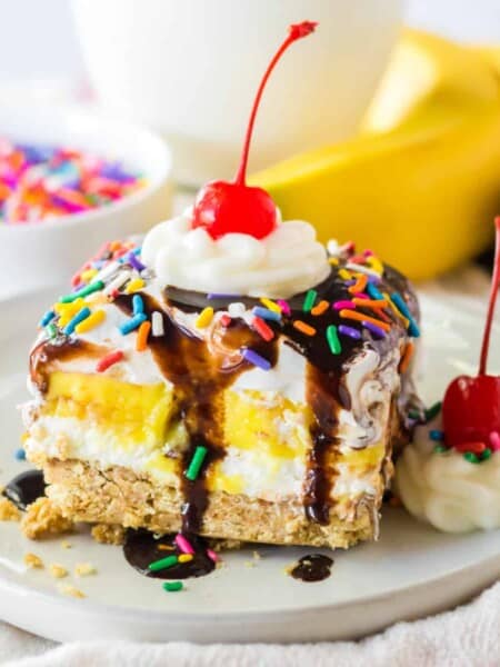 No bake banana split dessert with a graham cracker crust; layers of sweetened cream cheese, banana pudding, and Cool Whip; and topped with chocolate syrup, whipped cream, and a cherry.