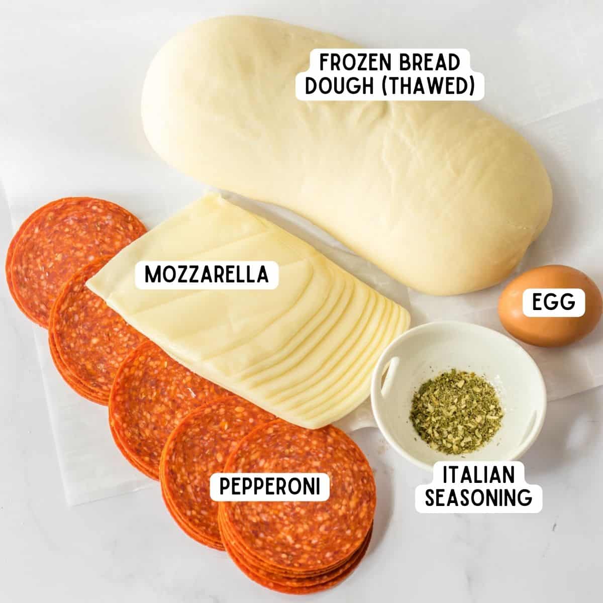Pepperoni bread ingredients: frozen bread dough (thawed), slices of mozzarella cheese, pepperoni, Italian seasoning, and an egg.