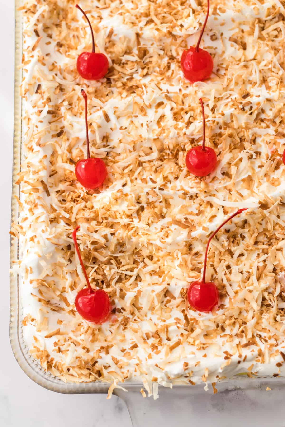 Pineapple Coconut dessert topped with toasted shredded coconut and cherries. 