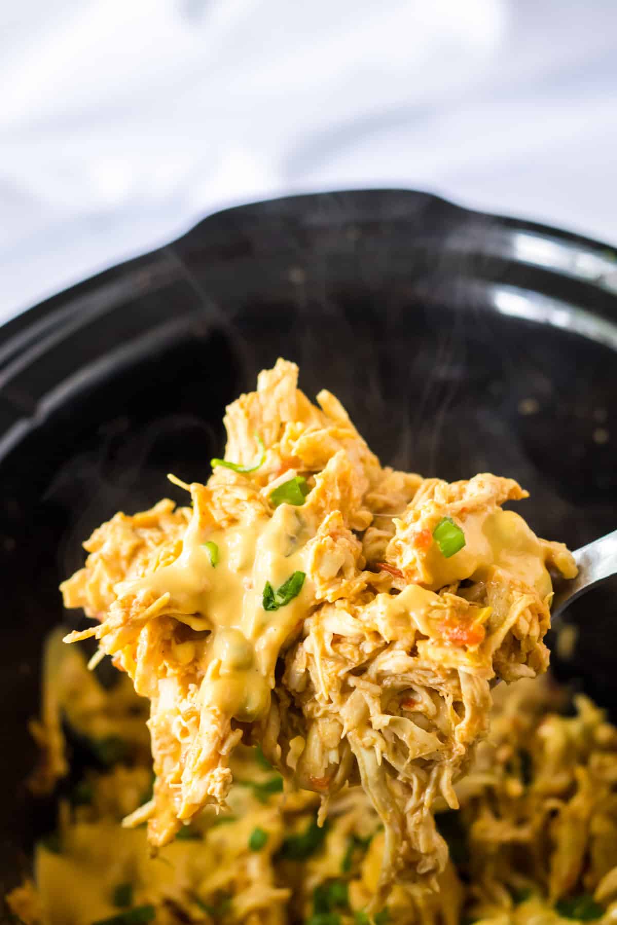 Spoon scooping queso chicken out of the slow cooker.