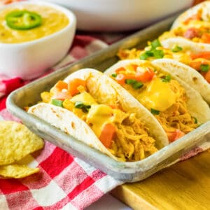 Slow cooker queso chicken tacos in flour tortillas on a serving tray.