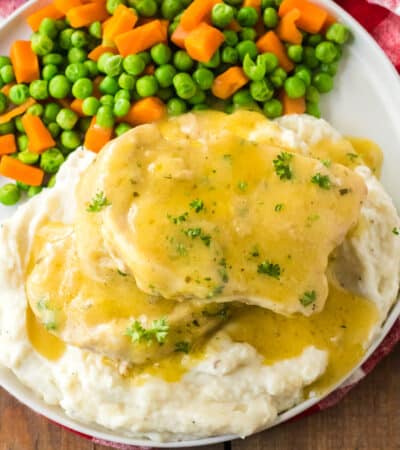 Pork chops smothered in gravy served over mashed potatoes and with a side of peas and carrots.