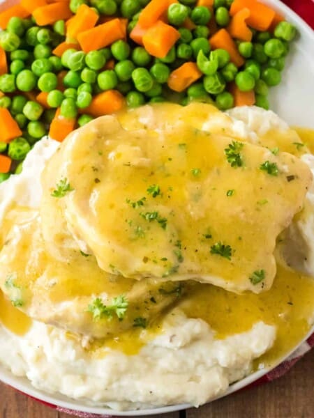 Pork chops smothered in gravy served over mashed potatoes and with a side of peas and carrots.