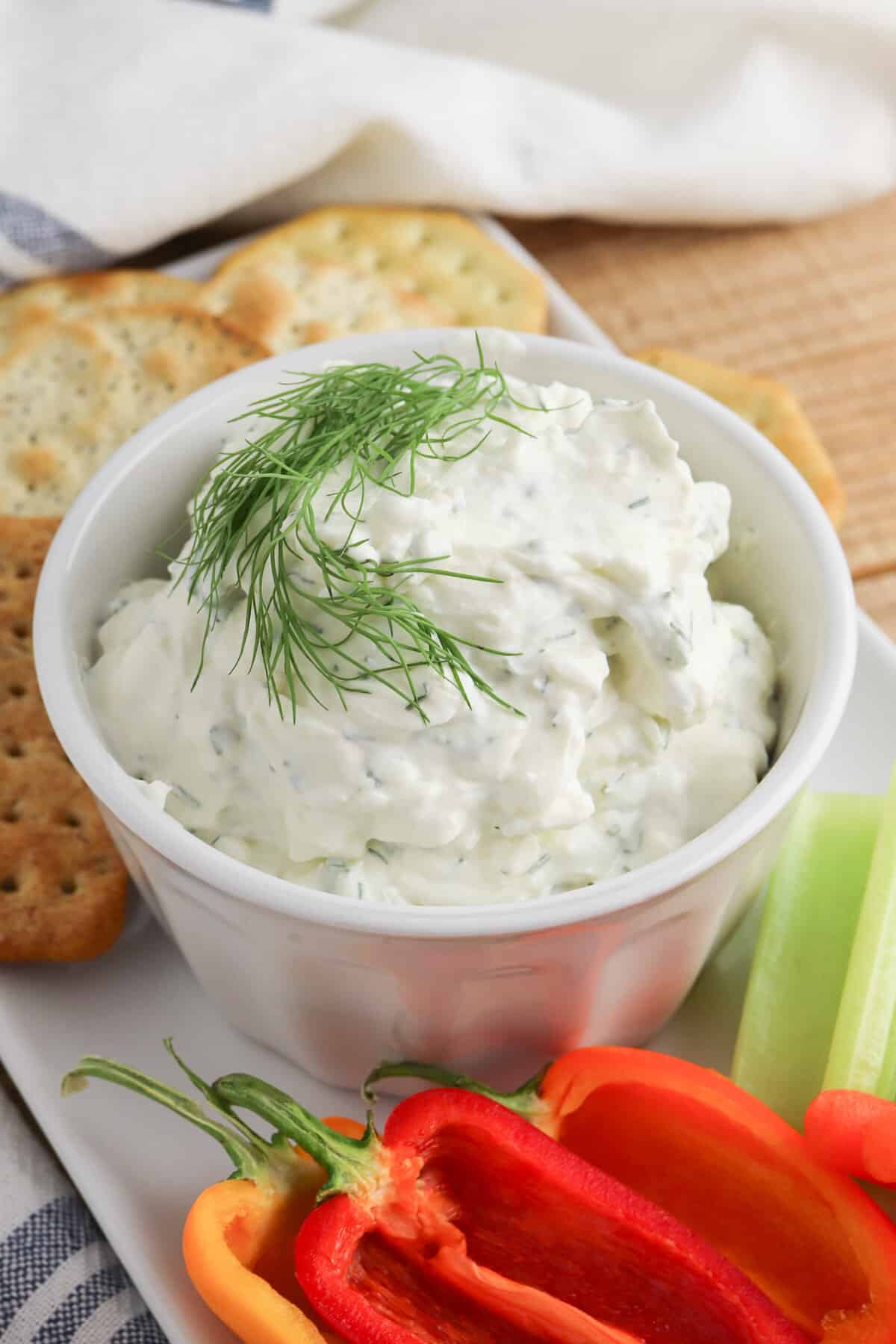 Cream cheese dill dip garnished with fresh dill sprig and served with crackers and fresh peppers and celery for dipping.