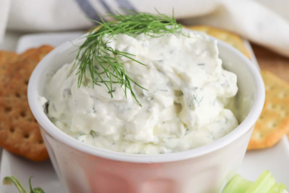Creamy dill dip garnished with a sprig of fresh dill and served in a bowl with crackers for dipping.