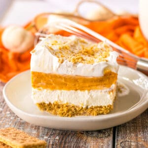 No bake pumpkin lush layered dessert with a graham cracker crust, sweetened cream cheese, pumpkin pie filling, vanilla pudding, and whipped topping.