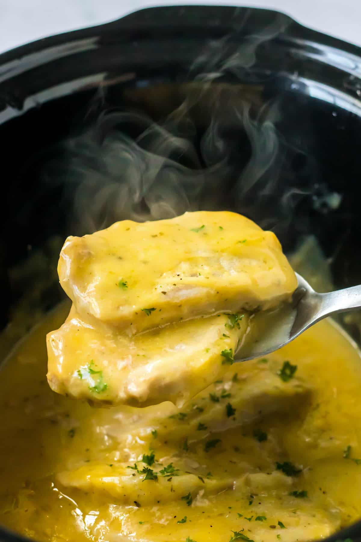 Steaming hot ranch pork chops being removed from the crock pot.