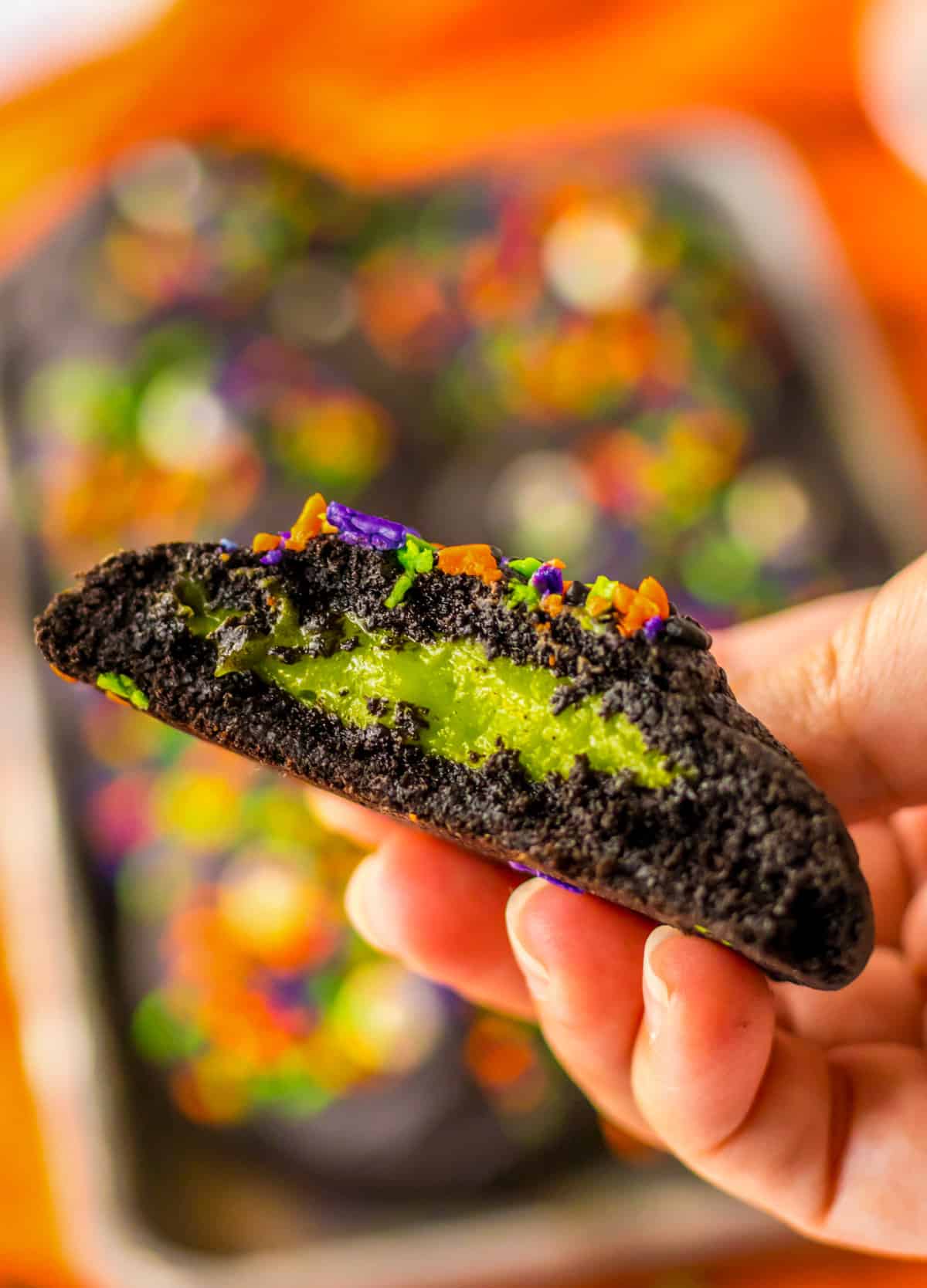 Hand holding a halloween cookie cut in half to show the neon green slime filling.
