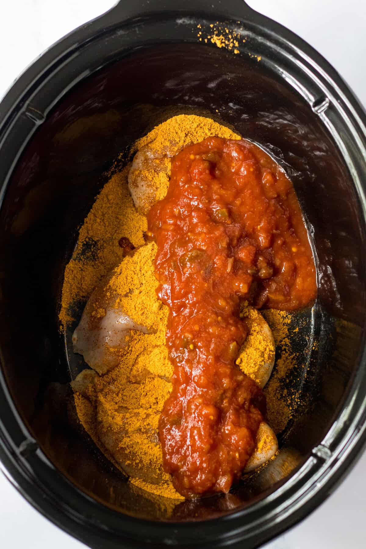 Chicken breasts in a crockpot topped with taco seasoning and salsa.