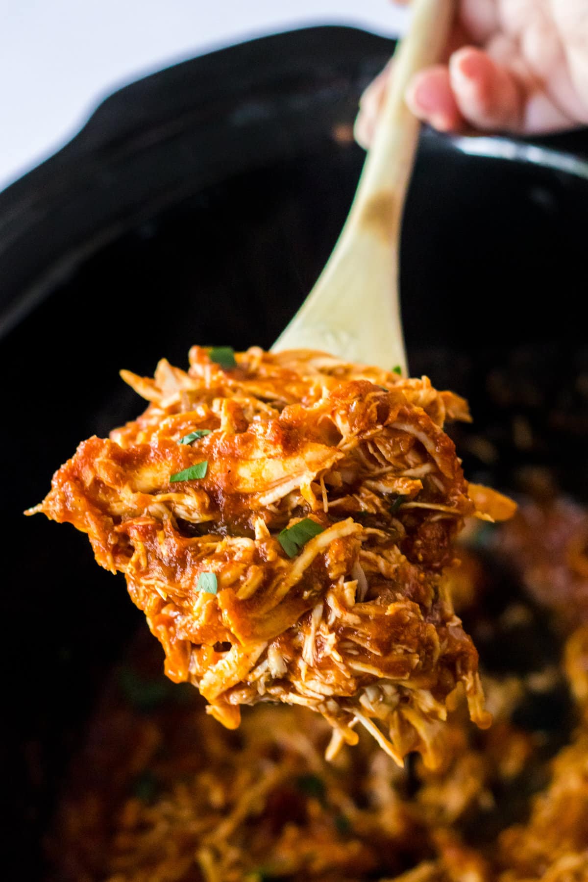 Wooden spoon scooping shredded salsa chicken from slow cooker.