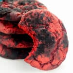 Red velvet cookies coated with black cocoa powder for a crinkle cookie effect. One cookie has a bite taken out of it to reveal the inside of the soft red velvet cake cookie.