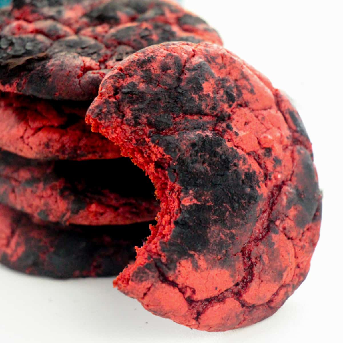 Red velvet cookies coated with black cocoa powder for a crinkle cookie effect. One cookie has a bite taken out of it to reveal the inside of the soft red velvet cake cookie.