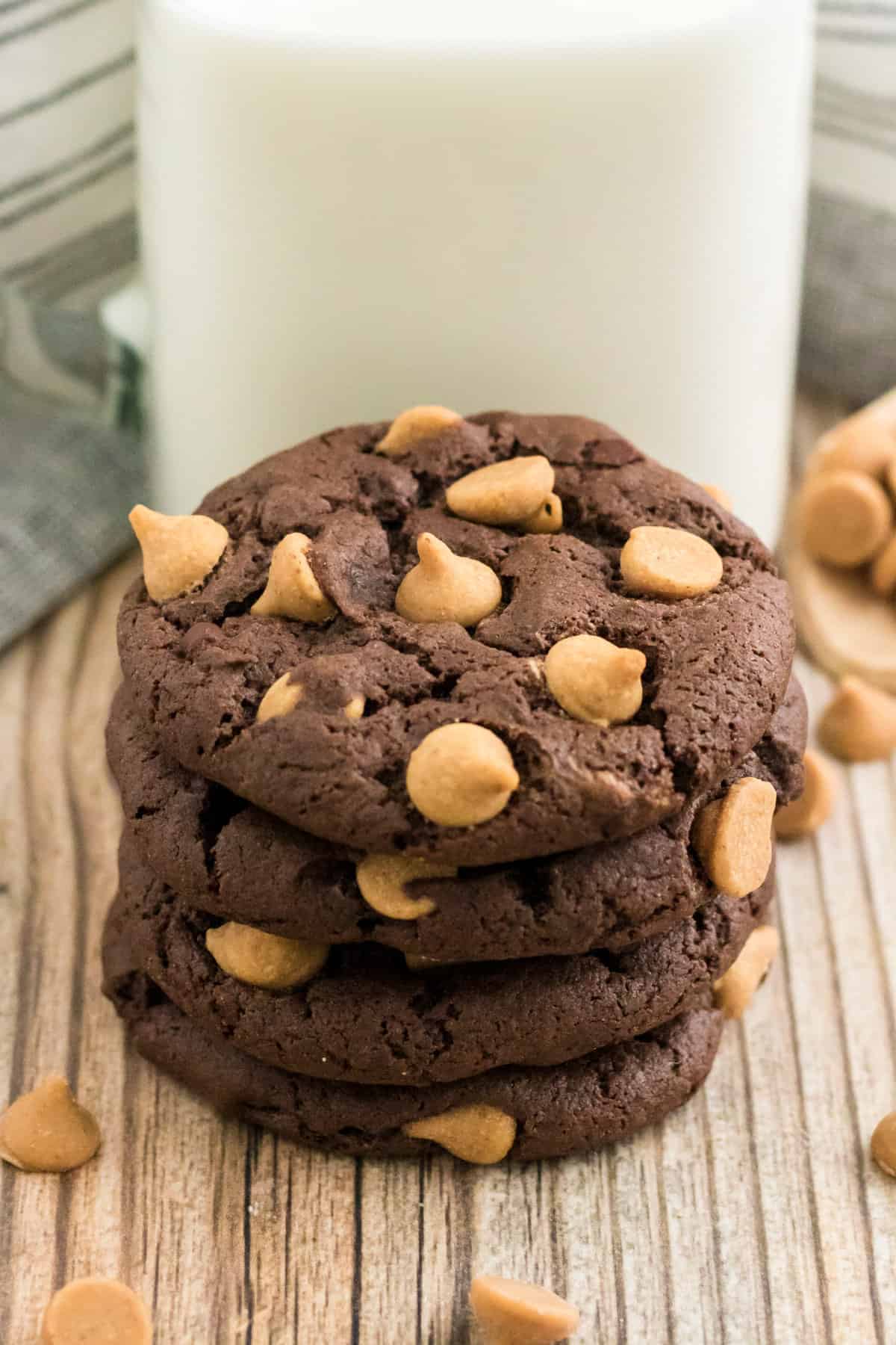 Chocolate cookies with peanut butter chips stacked on top of each other in front of a glass of milk.