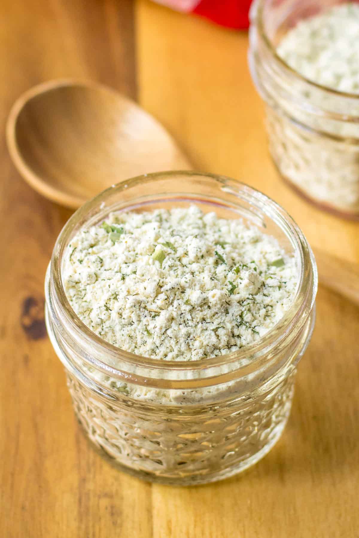 Homemade ranch seasoning mix in a glass jar with a wooden spoon next to it.