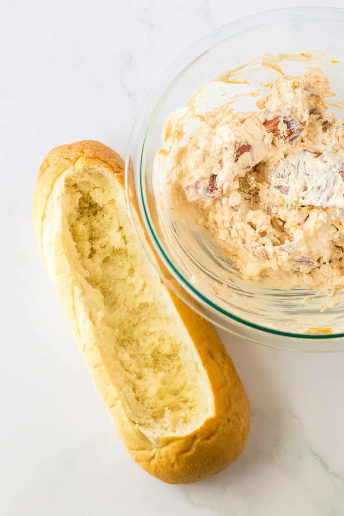 Hollowed out loaf of bread with bowl of bacon cheese dip next to it.