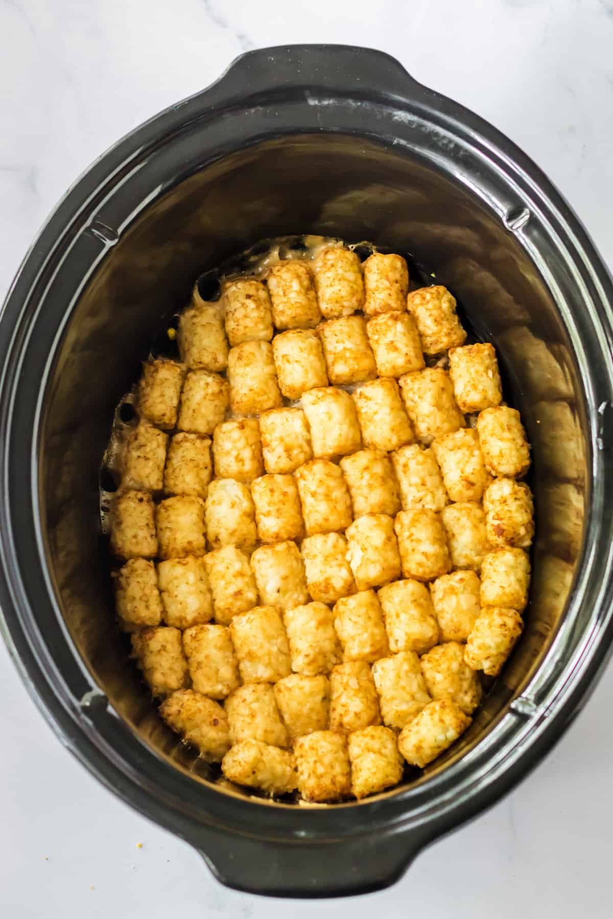 Tater tots in a neat and even layer in crock pot.