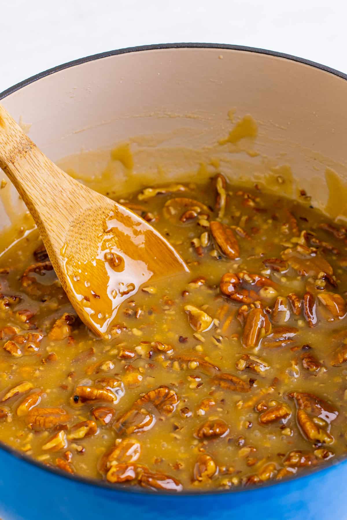 Wooden spoon in the pecan praline mixture in a blue dutch oven.