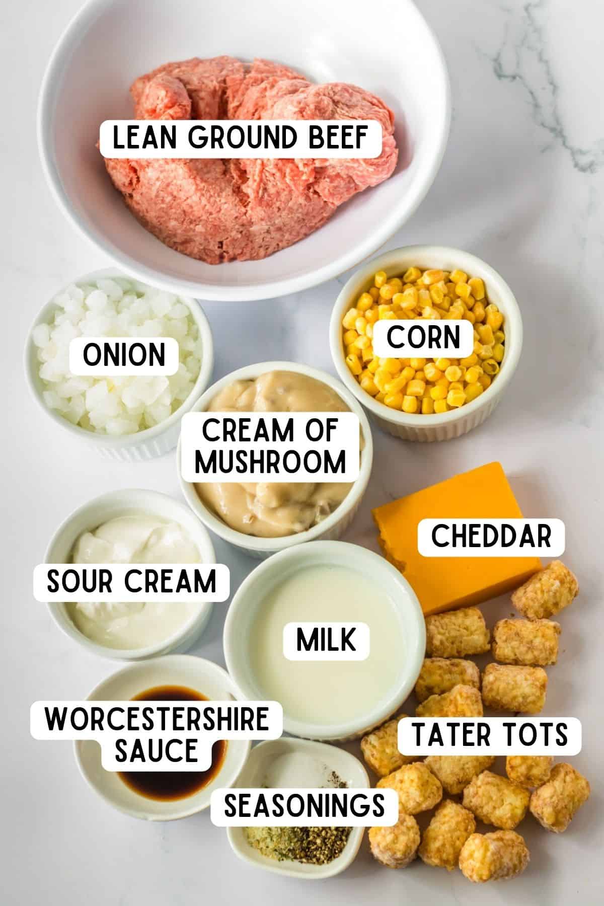 Ingredients for crock pot tater tot casserole:  lean ground beef, corn, onion, cream of mushroom, cheddar, sour cream, milk, worcestershire sauce, tater tots, and seasonings.