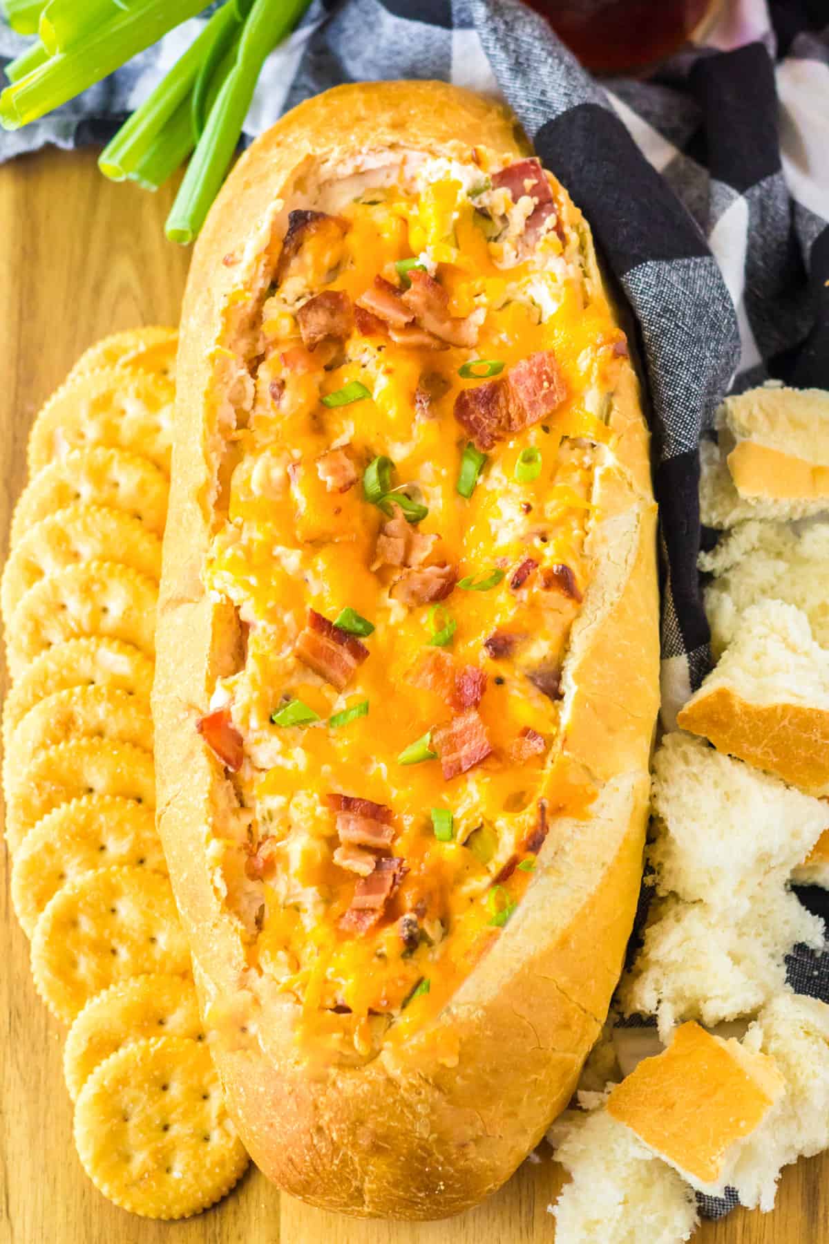 Mississippi Sin Dip with bacon, cheese, and scallions in a bread bowl, served with crackers and bread pieces for dipping.
