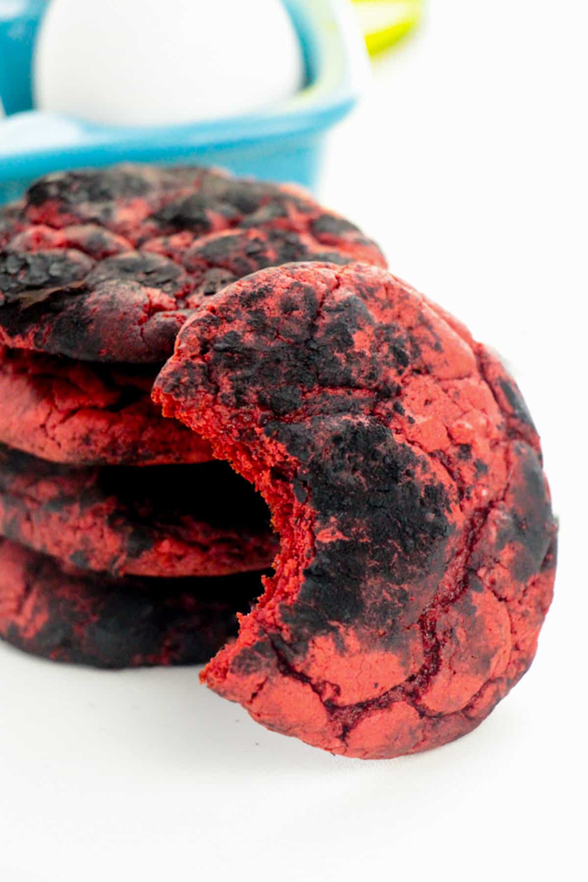 Red velvet cookies coated with black cocoa powder for a crinkle cookie effect. One cookie has a bite taken out of it to reveal the inside of the soft red velvet cake cookie.