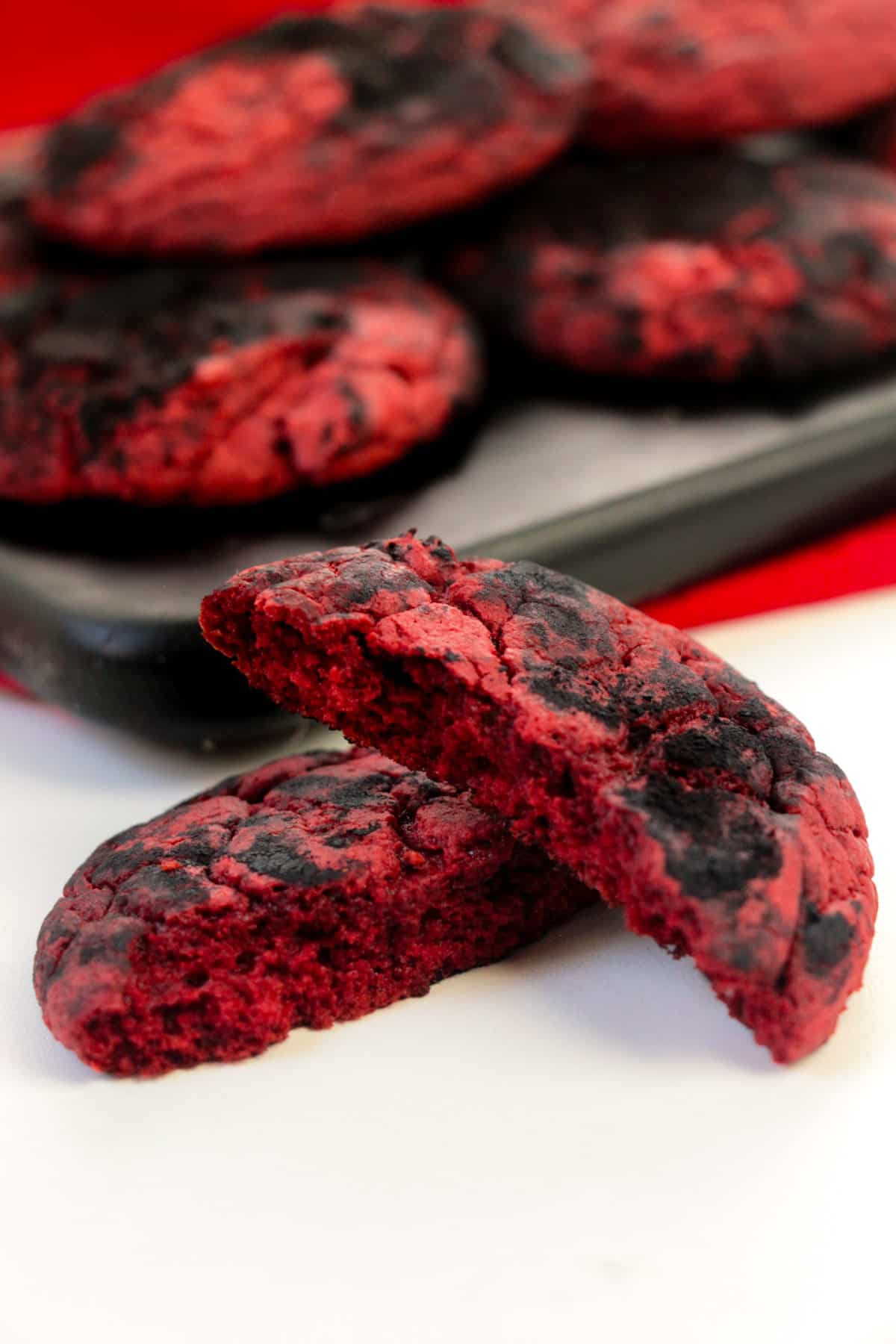 Red and black crinkle cookies on a wooden platter with one cookie broken in half to show red interior.