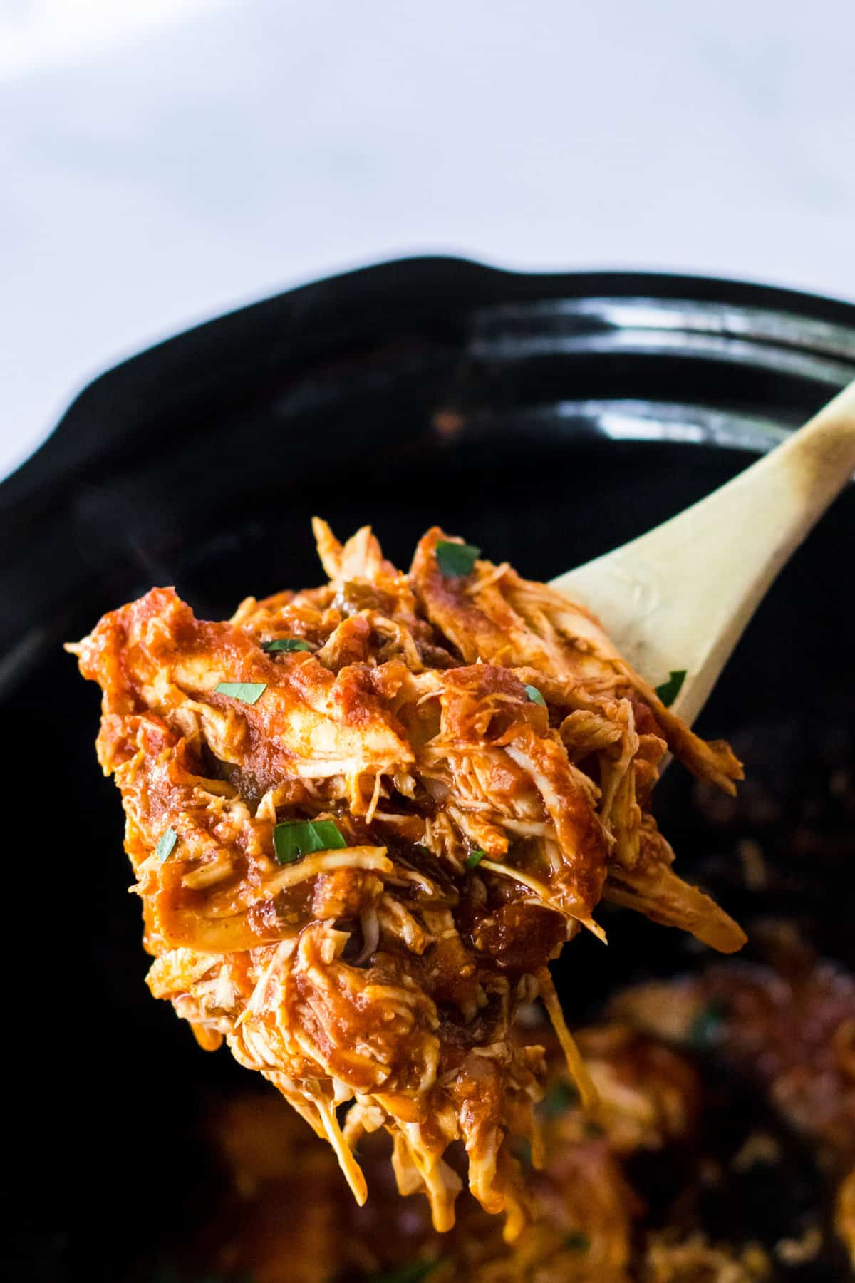 Shredded chicken breasts with salsa being scooped out of the slow cooker.