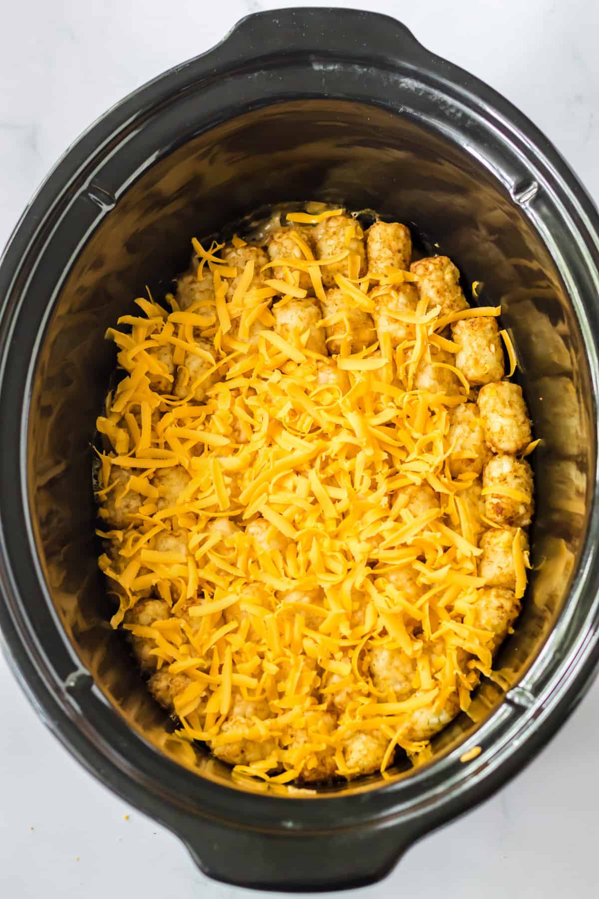 Shredded cheese on top of tater tot casserole in crockpot.