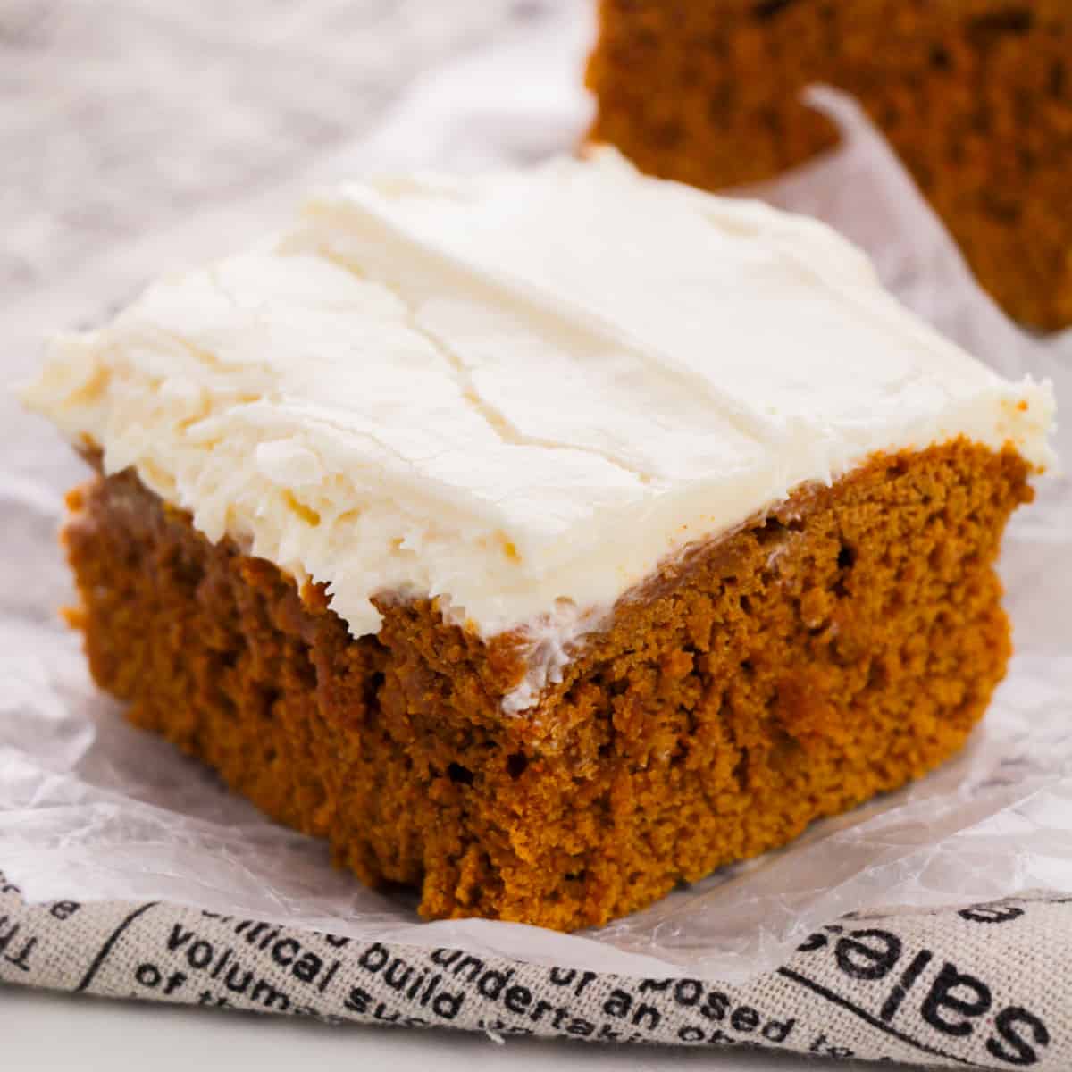 2-ingredient pumpkin spice cake with cream cheese frosting sliced into a square.