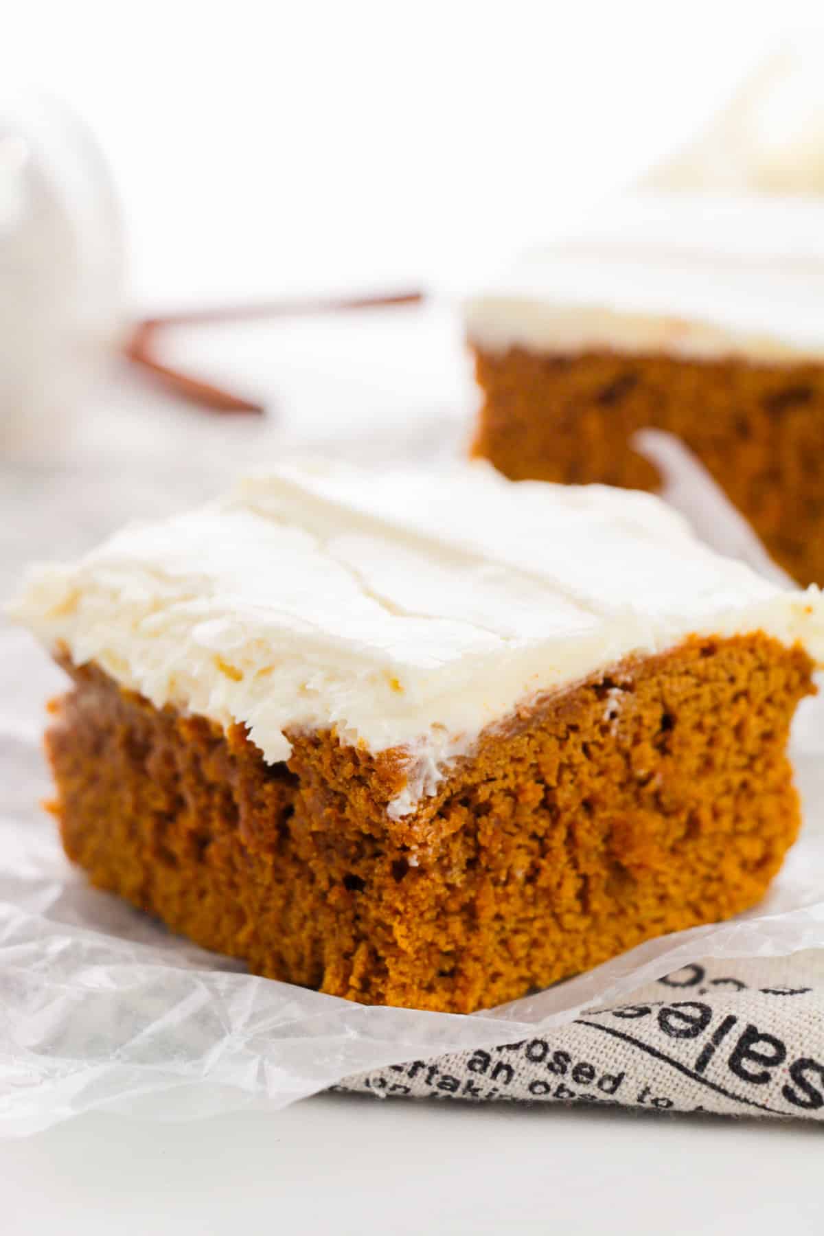 Square slice of ingredient pumpkin spice cake topped with cream cheese frosting.