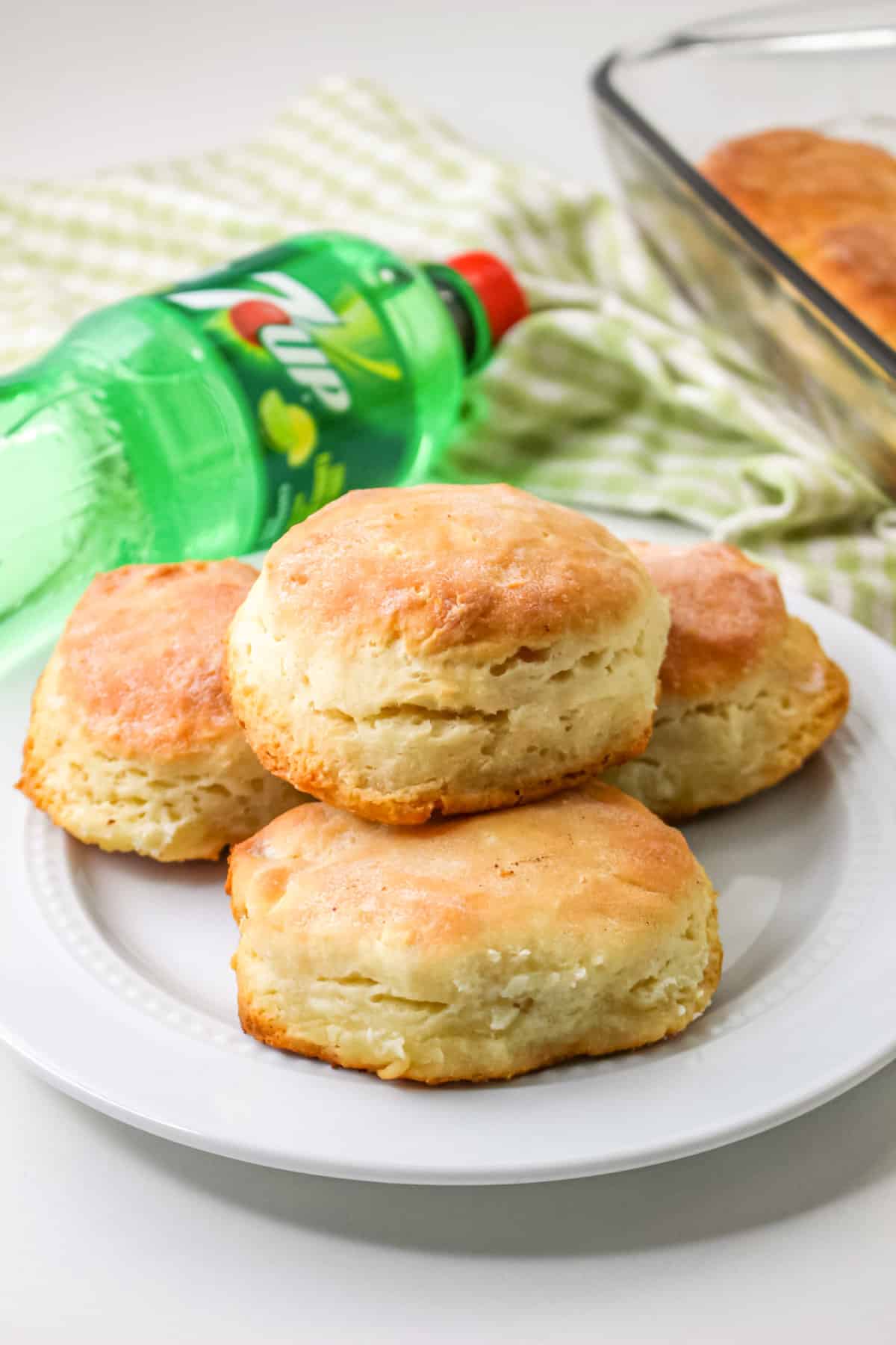4 soft and fluffy 7 up biscuits on a plate with a bottle of 7 up soda in the background.