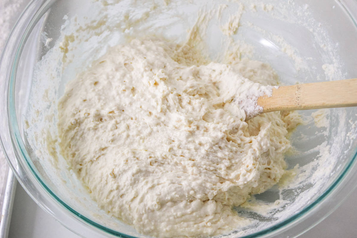 Soft and sticky biscuit dough in glass bowl with wooden spoon.