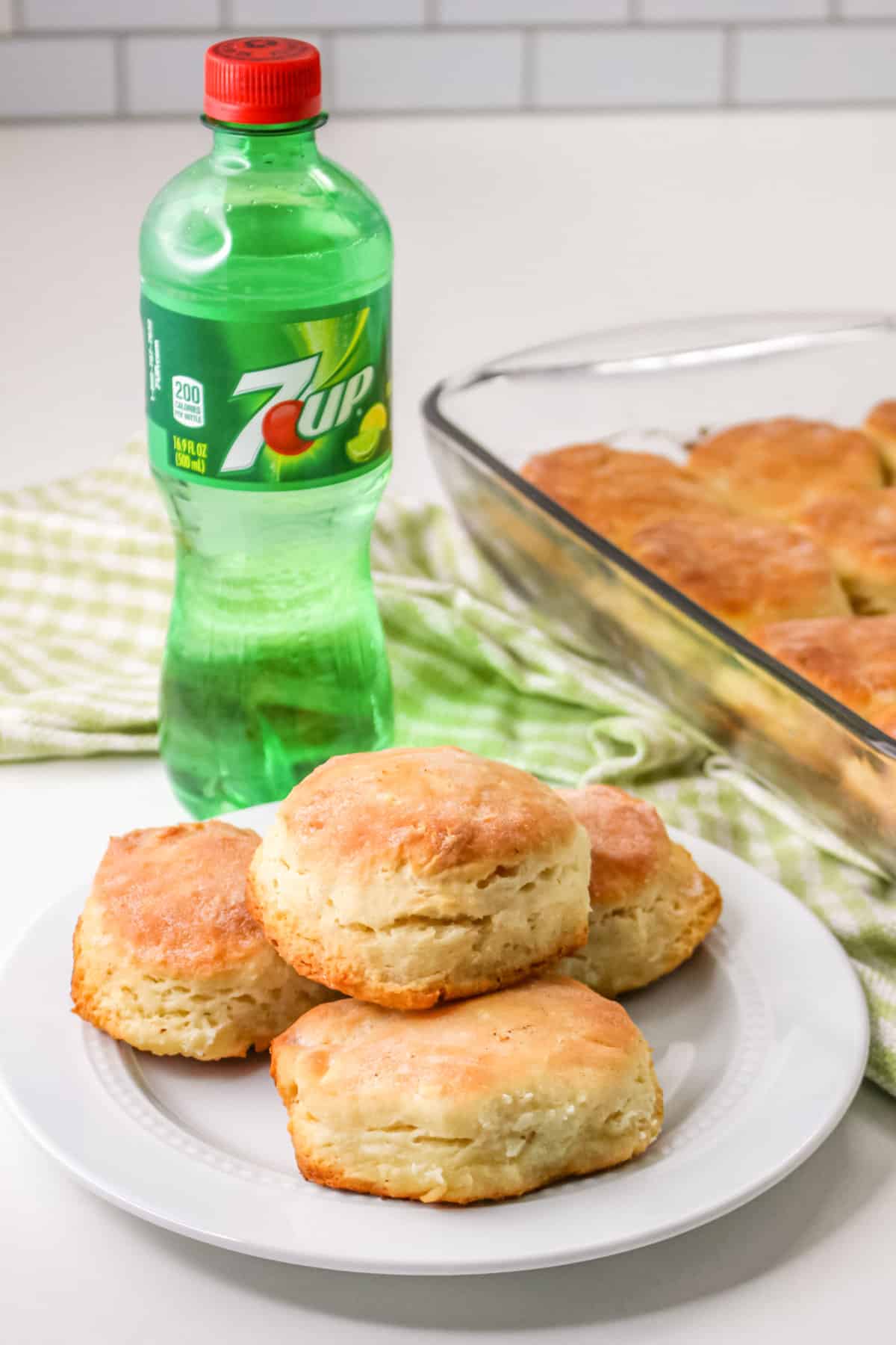 4 Bisquick 7 up biscuits on a plate next to the rest in a baking dish and a bottle of 7 up soda. 