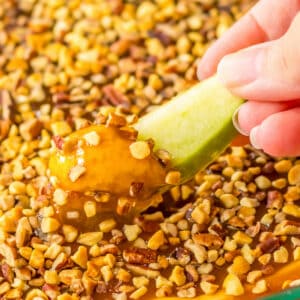 Green apple slice being dipped in cream cheese caramel apple dip.