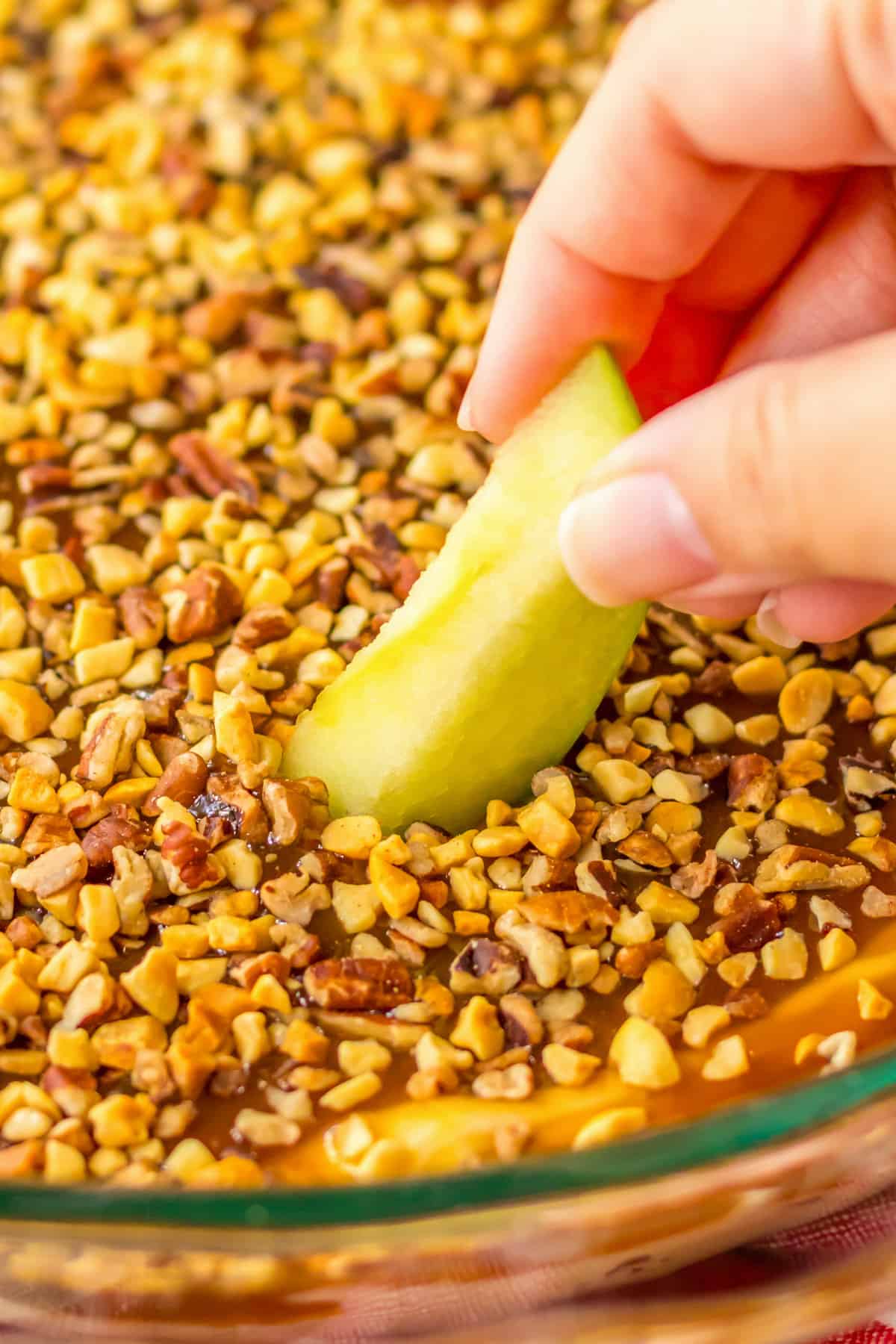 Dipping slice of green apple in cream cheese caramel apple dip.