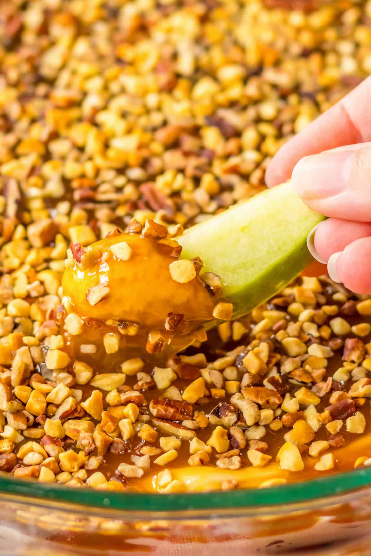 Green apple slice being dipped in cream cheese caramel apple dip.