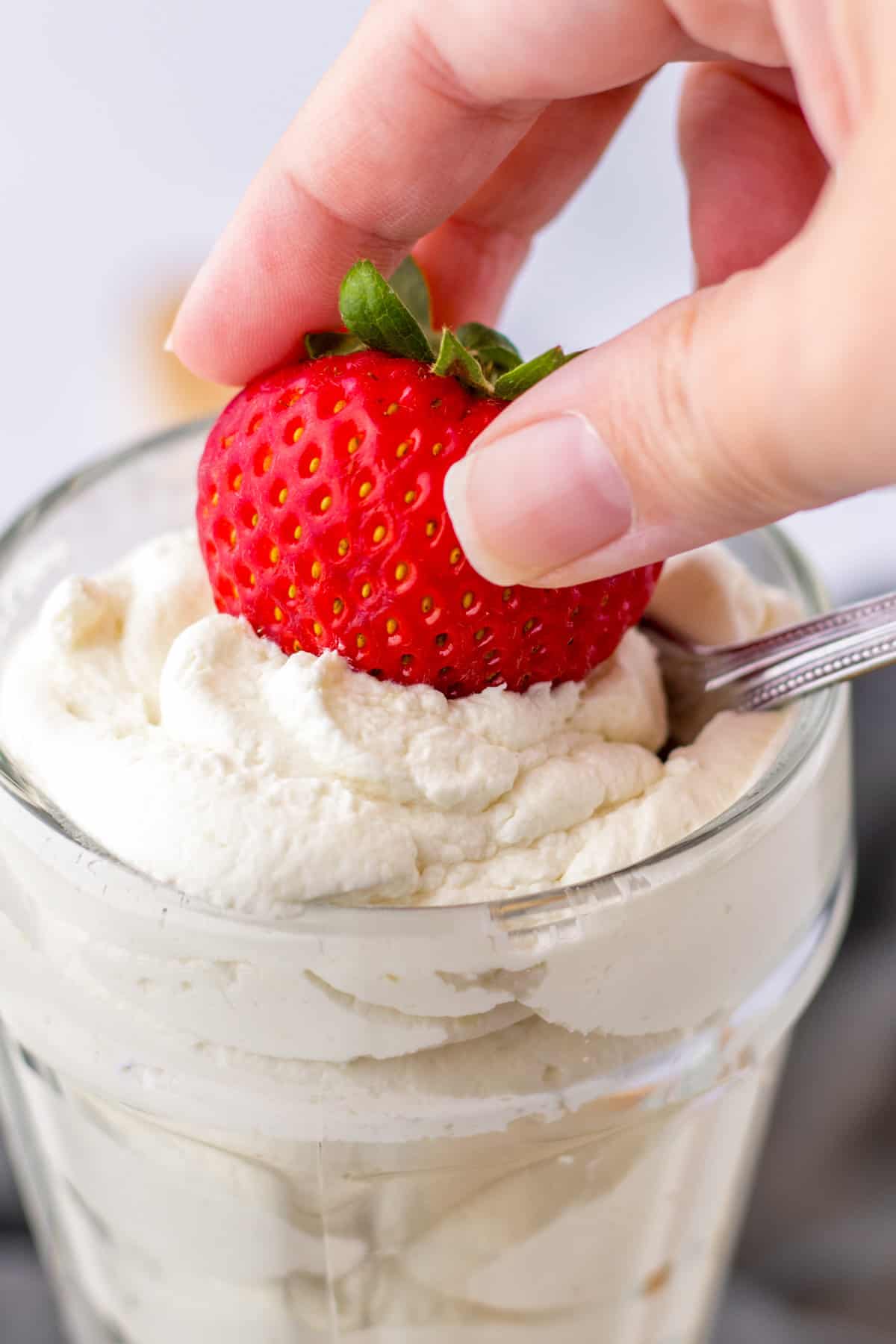 A fresh strawberry being dipping into homemade cool whip.