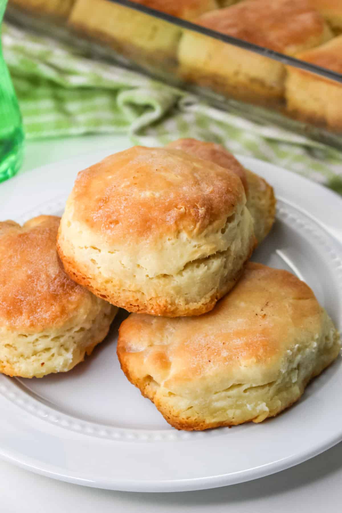 Fluffy 4-ingredient biscuits on white plate being baking pan of biscuits in background.