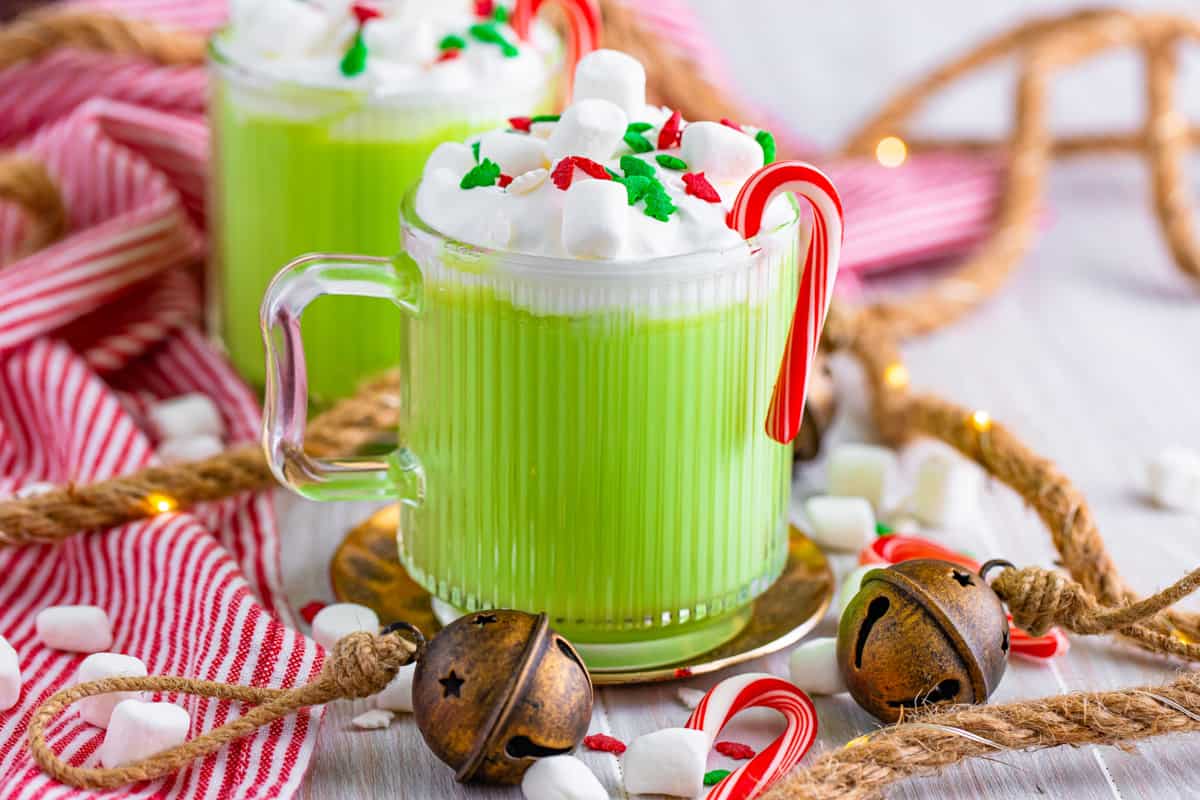 Green hot chocolate garnished with whipped cream, marshmallows, a candy cane, and sprinkles.