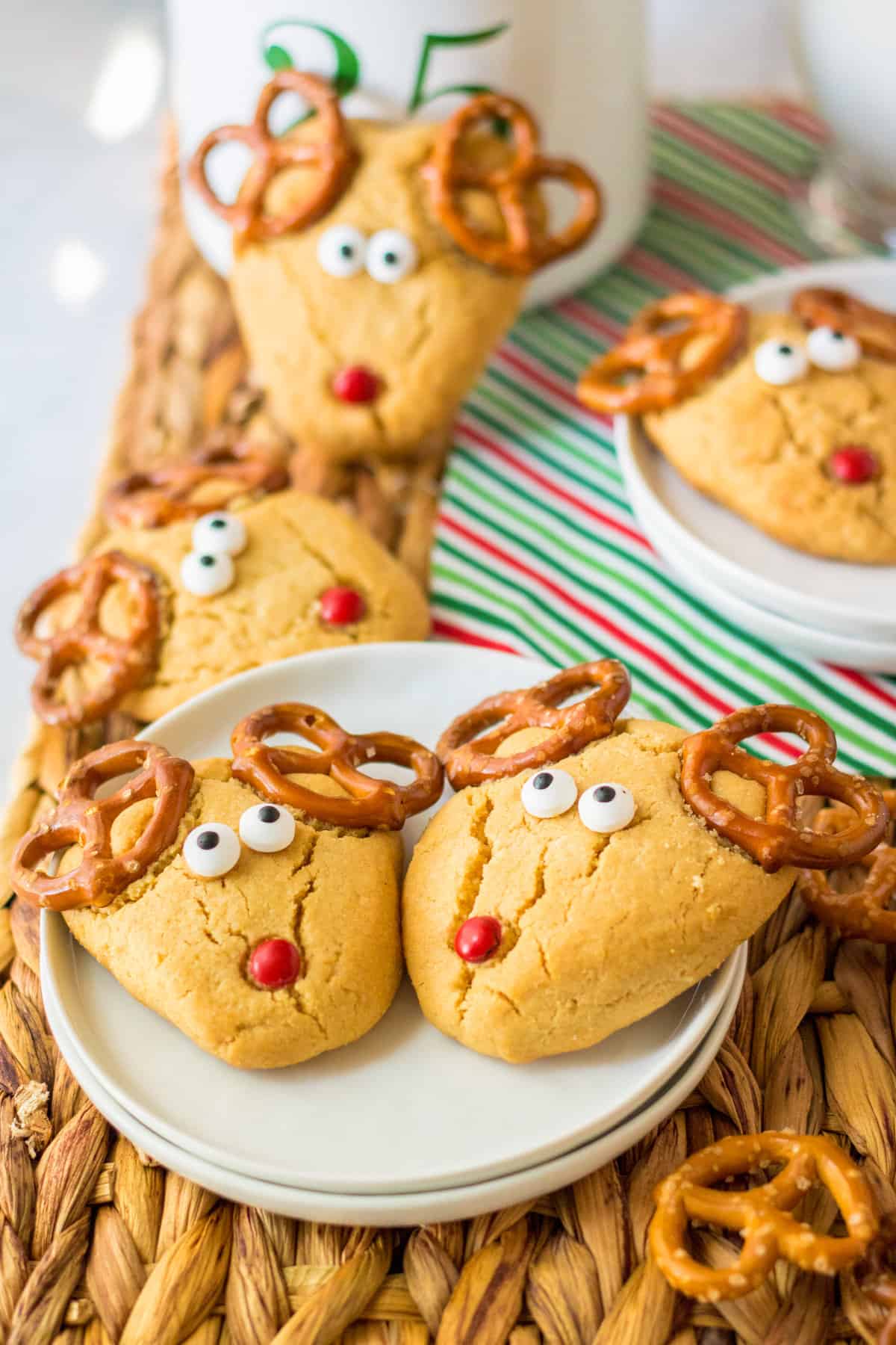 Peanut butter cookies shaped into an upside down triangle and decorated to look like Rudolph with pretzel antlers, candy eyes, and a red nose.