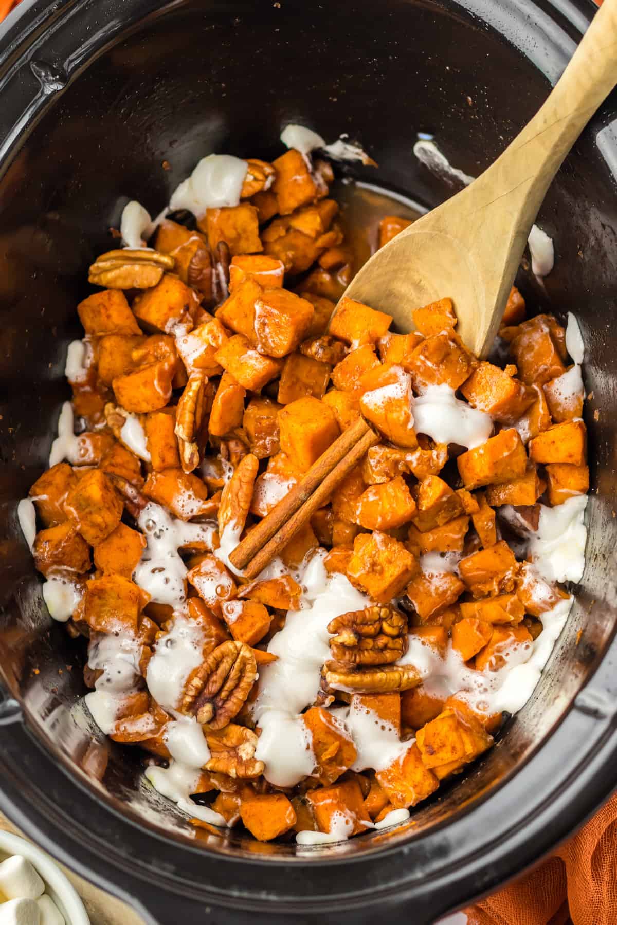 Crockpot sweet potato casserole with wooden spoon in it and leaning on the side of the insert.