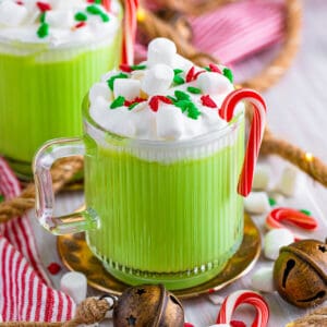 Slow cooker green grinch hot chocolate in a glass mug with whipped cream, mini marshmallows, christmas sprinkles, and candy canes.