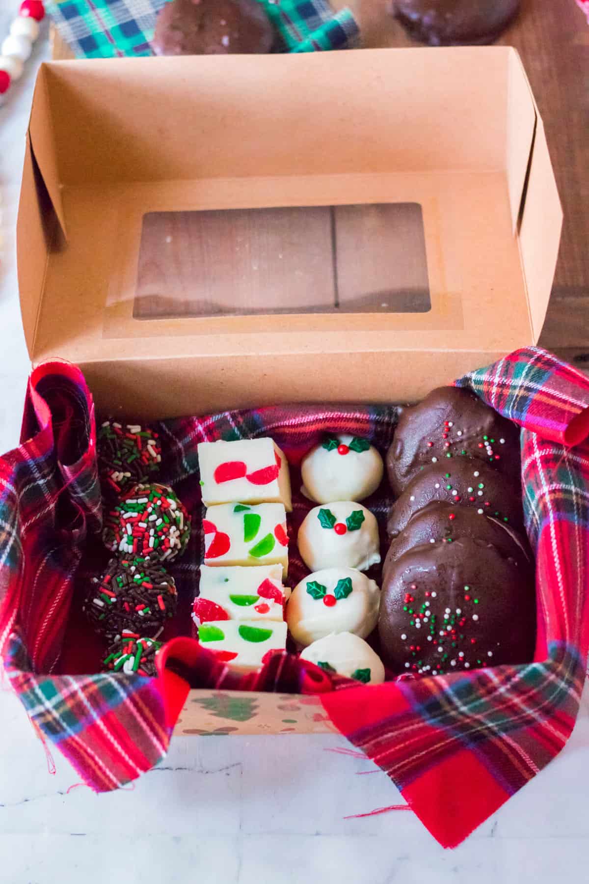 Box of homemade christmas candy ready for gifting. Contains: rum balls, gumdrop fudge, gingerbread truffles, and homemade peppermint patties.