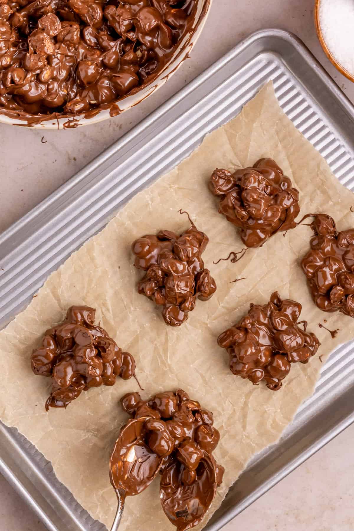 Clusters of candy being scooped onto lined baking sheets with two spoons.
