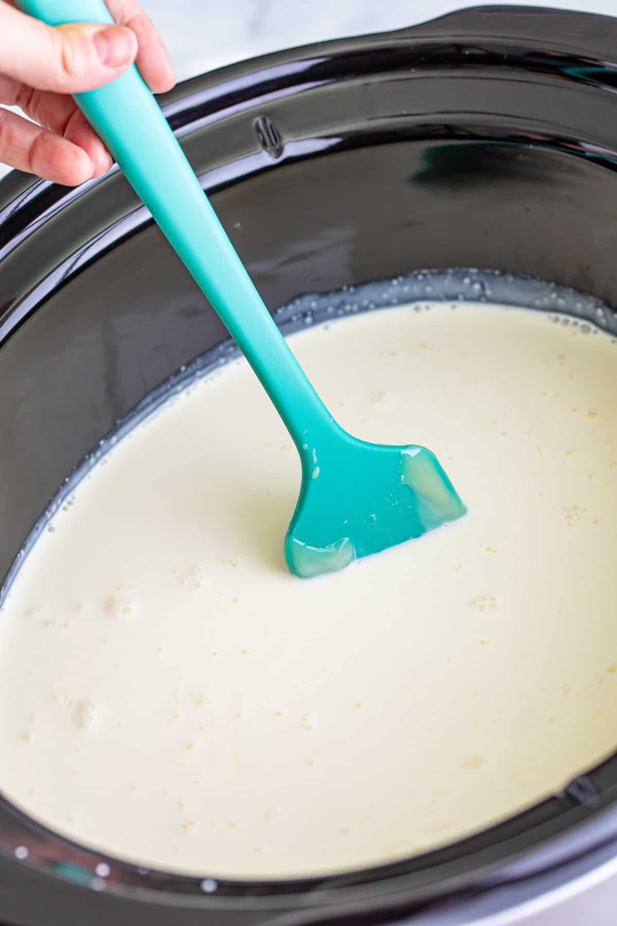 White hot chocolate being stirred with a rubber spatula in a slow cooker.