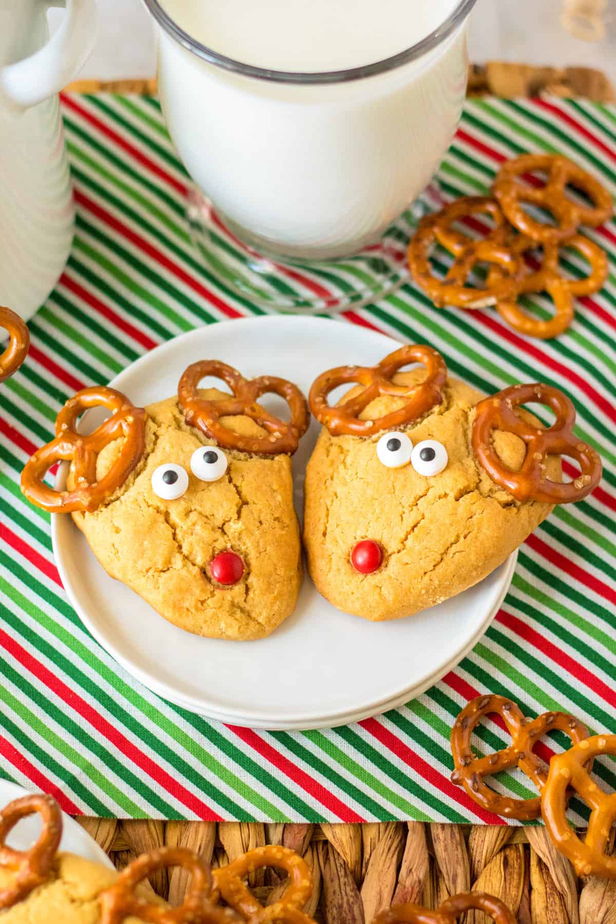 Two peanut butter reindeer cookies on a white plate with a large glass of milk.