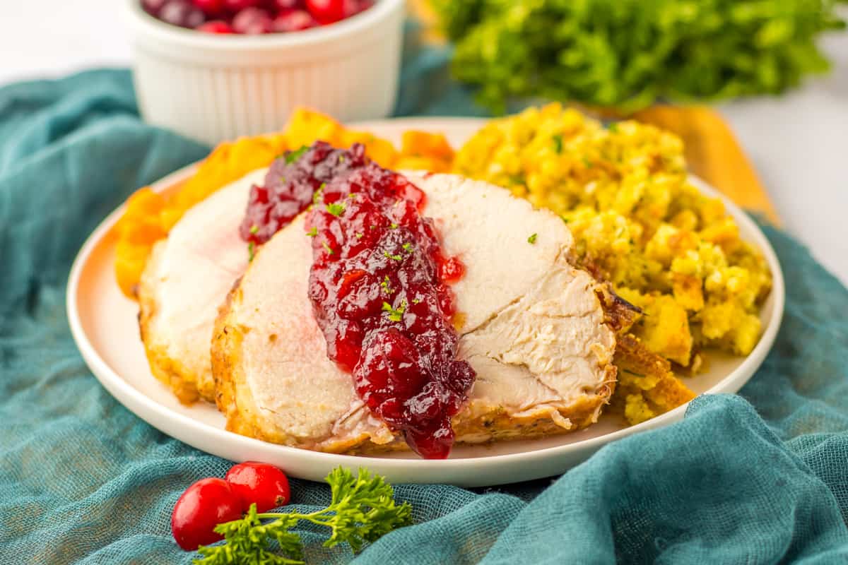 Sliced slow cooker turkey breast roast with cranberry sauce poured over the top and served with stuffing and sweet potatoes.