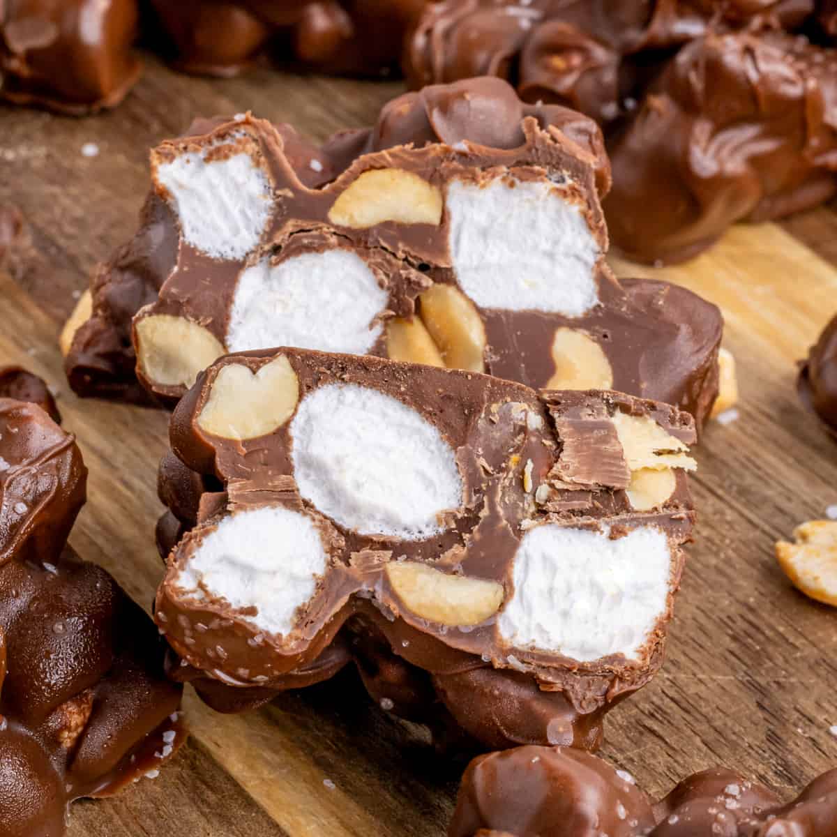 Rocky road candy on cutting board with one cut in half to show the marshmallows and peanuts inside in the chocolate clusters.