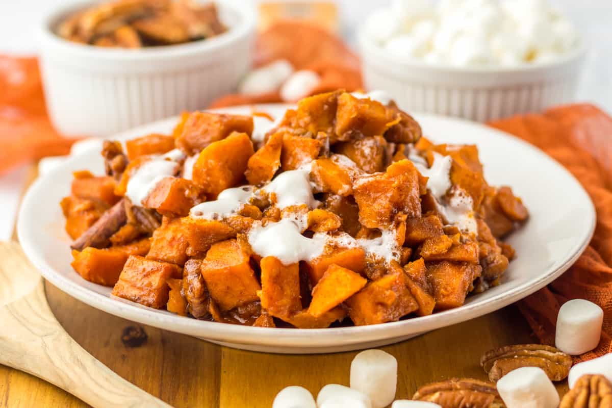 Sweet potatoes with pecans, brown sugar, and marshmallows on a white serving plate.